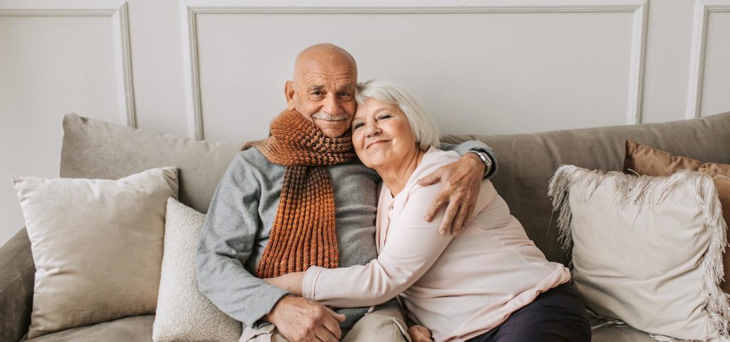 happy elderly couple hugging while sitting on a couch